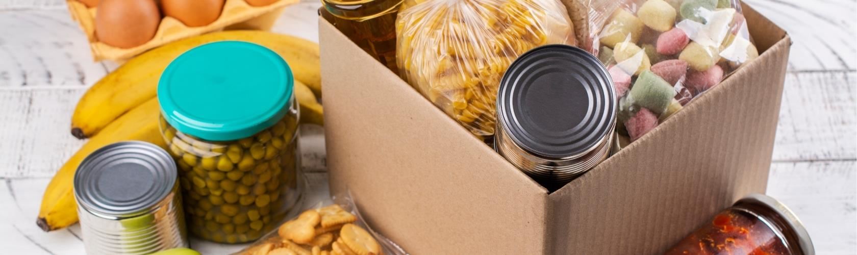 food items like bananas, crackers, eggs, canned goods on a table with pasta, cans, and other foods in a box